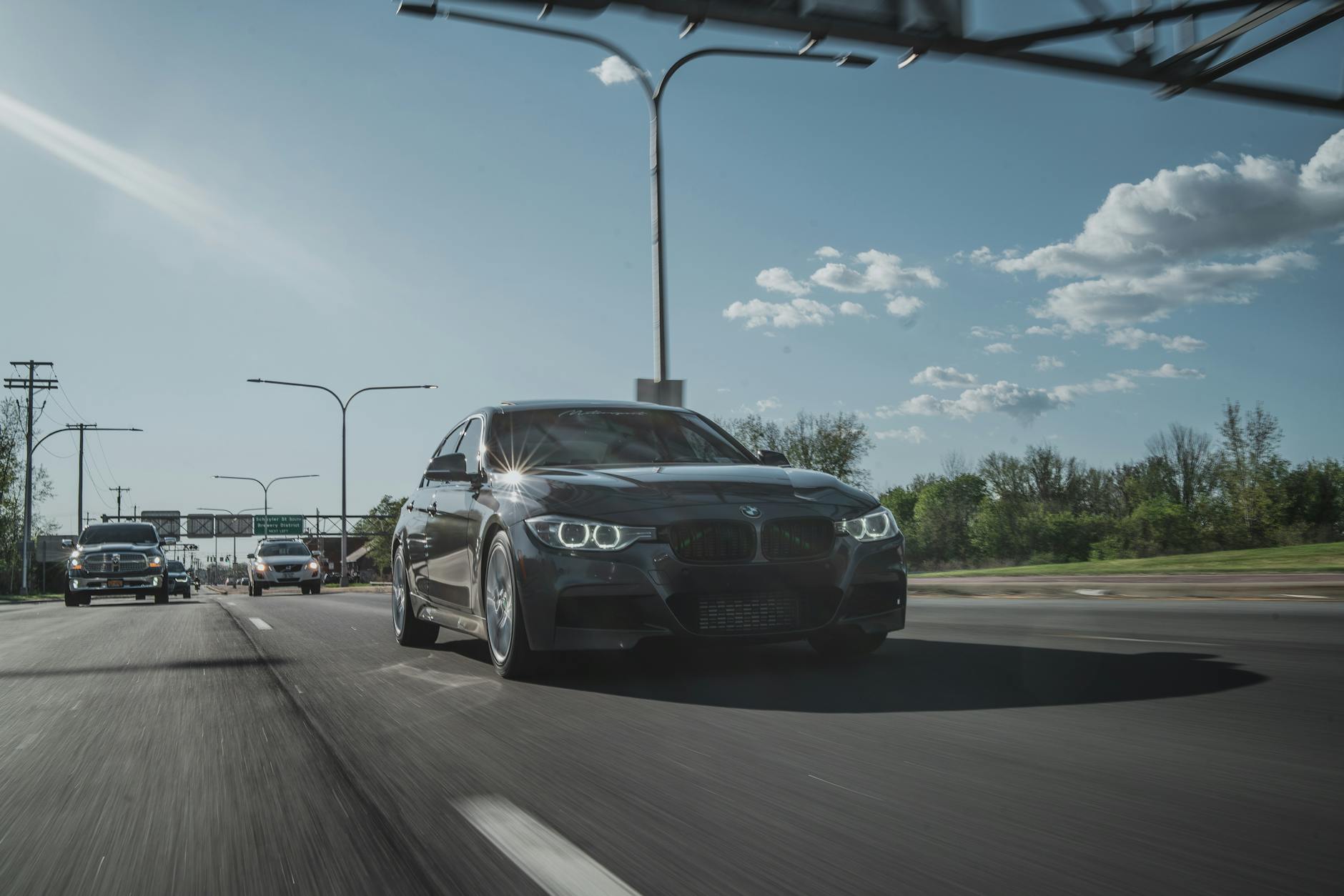 A black sedan driving down a sunny highway, showcasing dynamic motion and speed.